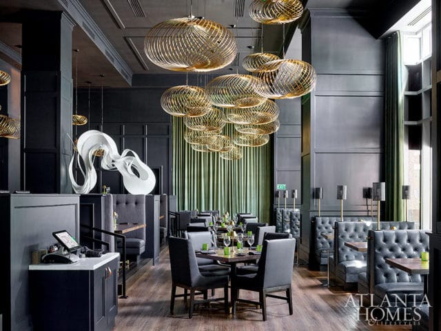 Restaurant dining room with dark walls, tufted booths, and gold pendant lights.