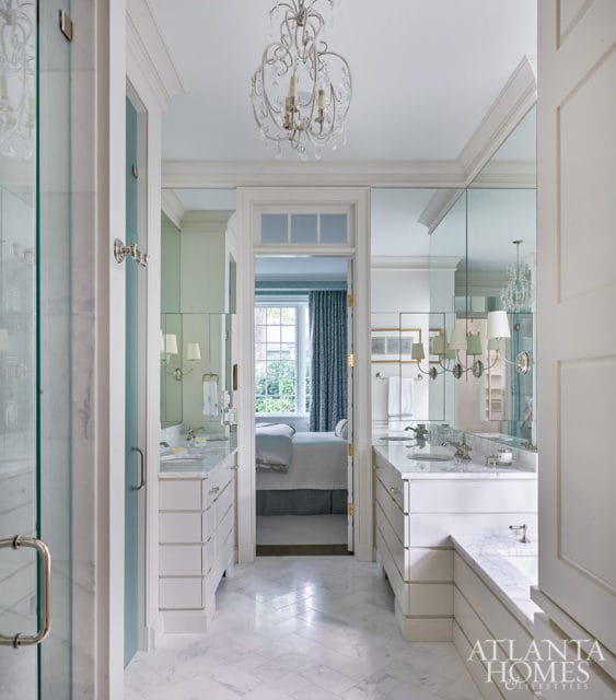 White bathroom with marble floors, dual vanities, and a view into a bedroom with blue curtains.