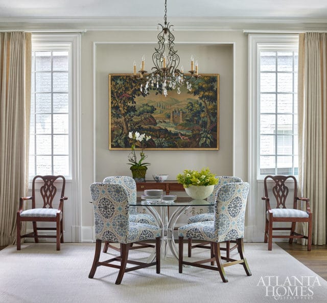 Dining room with glass table, upholstered chairs, and landscape tapestry