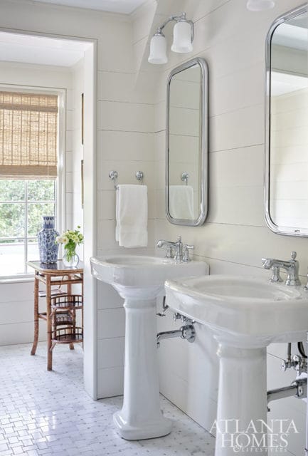 White bathroom with two pedestal sinks, shiplap walls, and marble tile floor.