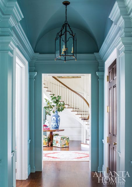 Hallway with teal walls, vaulted ceiling, and a black lantern chandelier. A curved staircase is