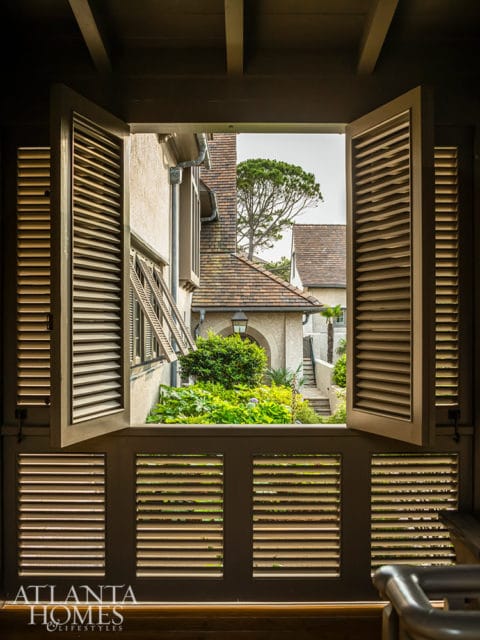 View through open shutters to a lush garden and courtyard with stone steps.
