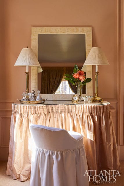 Vanity table with draped skirt, mirror, two lamps, and floral arrangement.