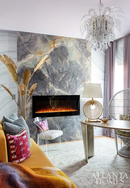 Living room with marble fireplace, yellow sofa, acrylic chair, and gold palm leaf decor.