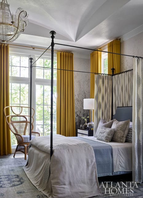 Primary bedroom with a four-poster bed, yellow curtains, and a wicker chair.