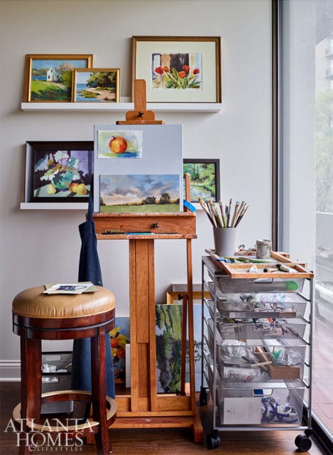 Artist's studio with easel, paintings, art supplies, and a leather stool.