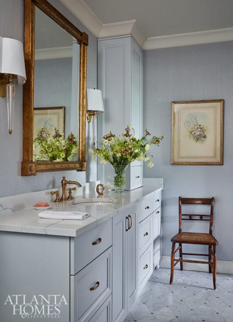 Light blue vanity with marble countertop, brass faucet, and gold mirror.