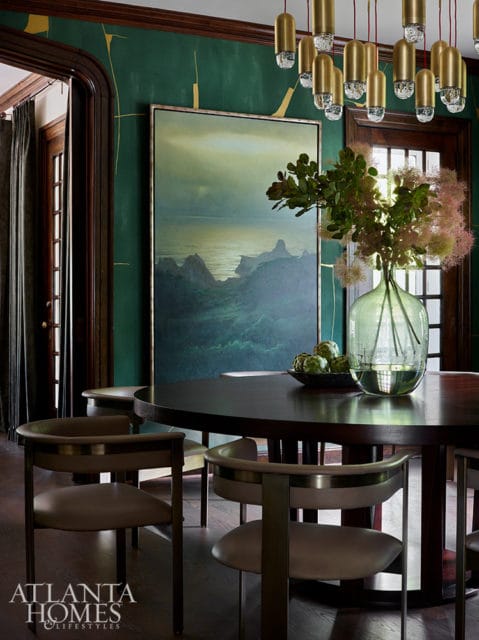 Dining room with dark wood table, upholstered chairs, green walls with gold accents, and landscape