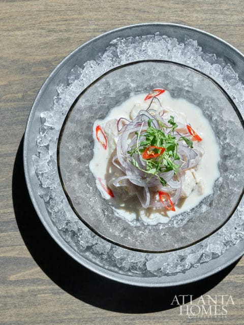 Ceviche with red onion, chili, and microgreens on ice in a metal bowl.