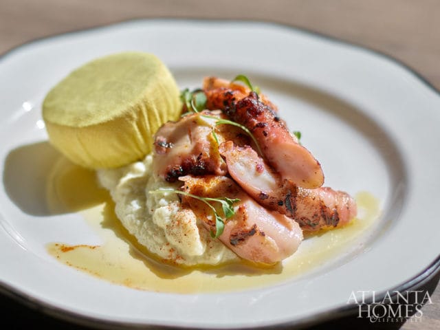 Grilled octopus tentacles served over mashed cauliflower with a yellow round garnish.