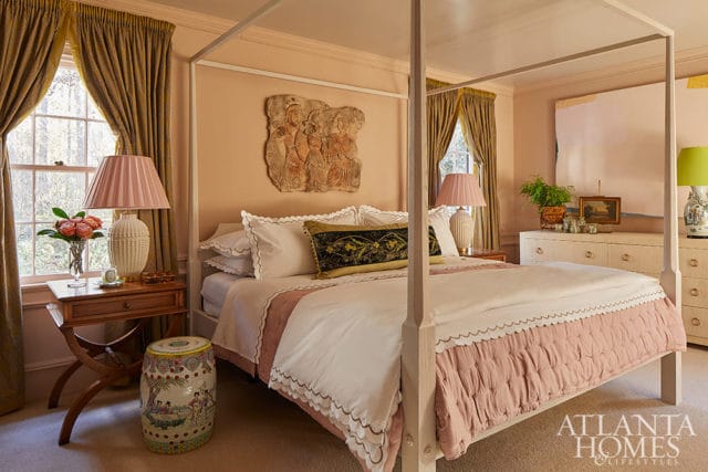 Bedroom with a four-poster bed, pink and white bedding, gold curtains, and a stone relief on the