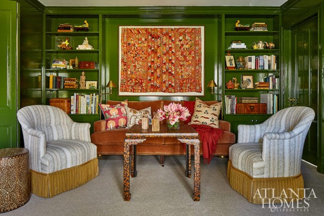 Green study with orange velvet sofa, patterned chairs with fringe, and ornate coffee table.