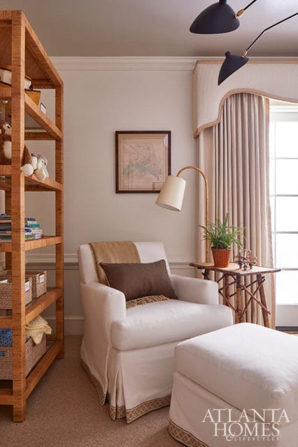 White armchair and ottoman with brown pillows and blanket, next to a rattan shelf and side table.