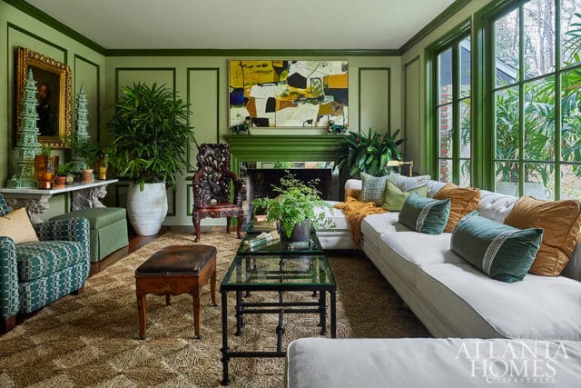 Green living room with white sectional sofa, patterned armchairs, ornate chair, and abstract art
