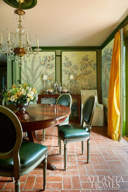 Dining room with green leather chairs, wooden table, brick floor, and chinoiserie wallpaper.