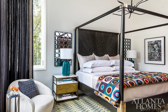 Bedroom with dark wood four-poster bed, colorful geometric blanket, and teal lamp.