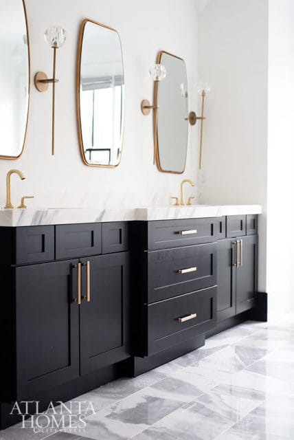 Black bathroom vanity with marble countertop, brass faucets, and mirrors
