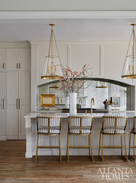 White kitchen with striped bar stools, brass accents, and glass pendant lights.