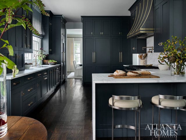 Dark blue kitchen with marble countertops, brass accents, and dark wood floors.