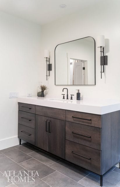 Dark wood vanity with white countertop, black fixtures, and arched mirror.