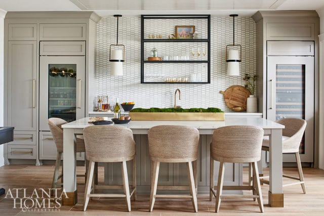 Light gray kitchen with marble island, woven bar stools, and wine fridge.