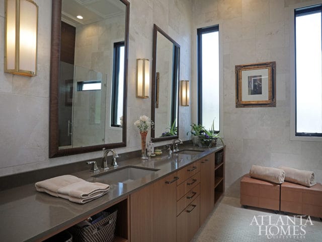 Double vanity with wood cabinets, stone countertop, and large mirrors. Two towels on ottomans.