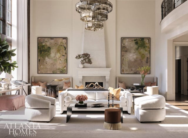 Living room with white sofa, two white armchairs, fireplace, and abstract art.