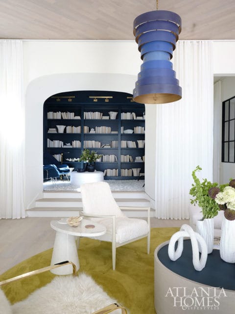 Living room with white chairs, yellow rug, and navy bookshelves.