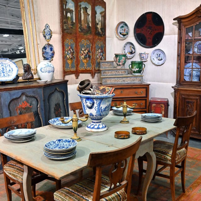 Dining table with blue and white plates, ornate vase, and wooden chairs.