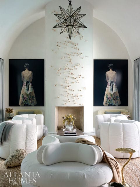 Living room with white curved sofas, starburst chandelier, and two portraits of women
