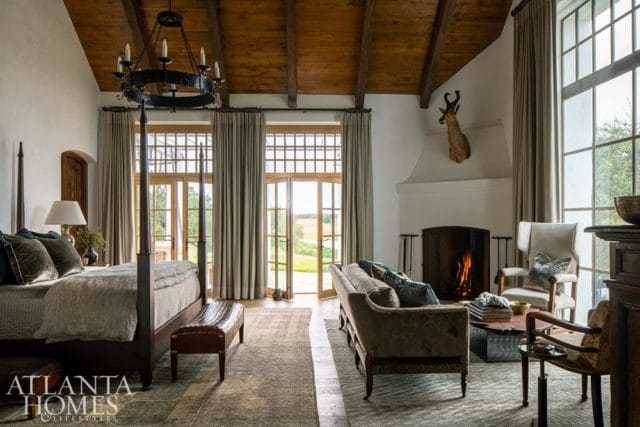 Bedroom with four-poster bed, fireplace, and seating area. Wood beams on ceiling.