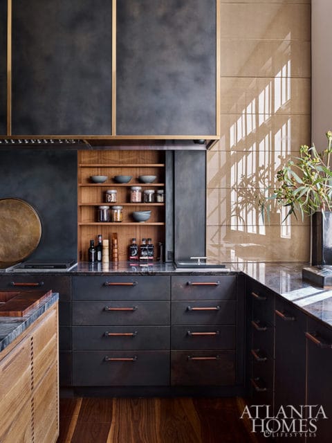 Dark gray kitchen cabinets with wood handles, open shelving with bowls and jars, and brass-trimmed