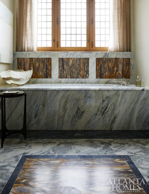 Marble bathtub with wood-framed window above and decorative marble panels.