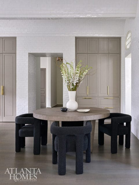 Round dining table with black bouclé chairs and white vase with flowers