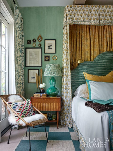 Bedroom with green walls, canopy bed, rattan chair, and patterned rug.