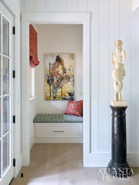 Built-in bench with striped cushion, abstract art, and wooden sculpture on pedestal.