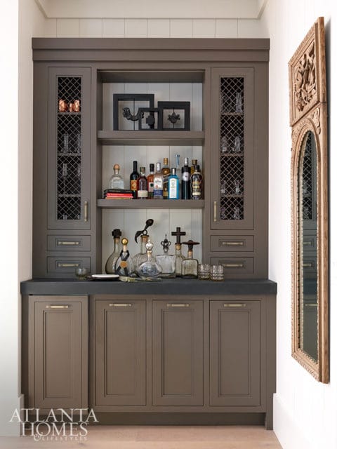 Gray built-in bar with glass-front cabinets, liquor bottles, and decorative items.