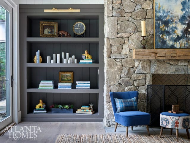 Gray built-in bookshelves with decorative items and a stone fireplace with a blue chair.