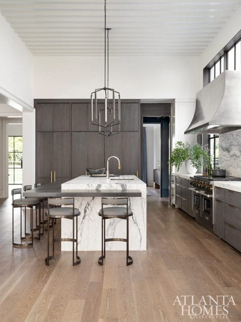 Modern kitchen with dark gray cabinetry, marble island, and pendant light.