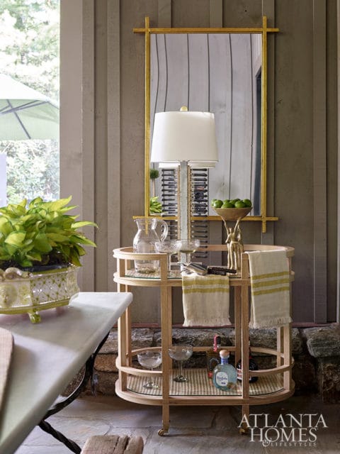 Bar cart with glassware, bottles, and towels, next to a marble-top table.