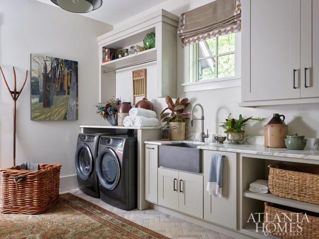 Laundry room with gray washer and dryer, farmhouse sink, marble counters, and woven baskets.