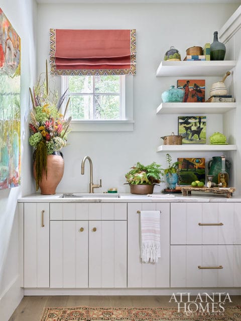 White cabinet bar with brass hardware, marble countertop, and sink. Shelves above hold decorative