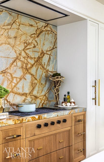 Kitchen with a dramatic stone backsplash, wood cabinetry, and brass hardware.