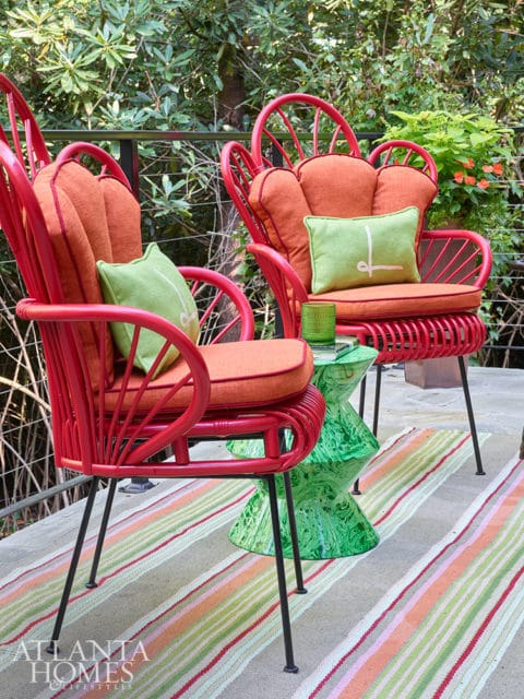 Two red wicker chairs with orange cushions and green pillows on a striped rug.