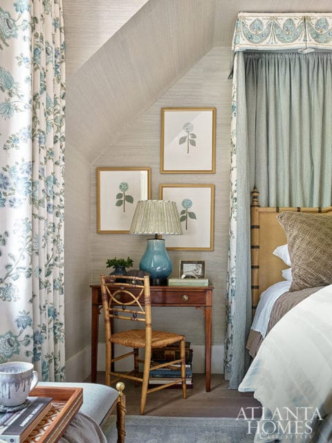 Bedroom with floral curtains, framed botanical prints, and a wooden desk with a blue lamp.