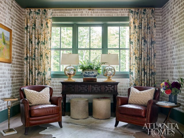 Two brown leather armchairs flank a dark wood console table with lamps and plants.