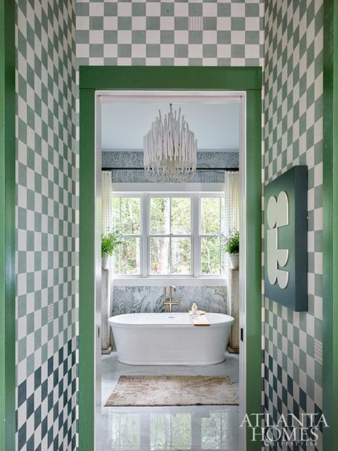 Bathroom with checkered green and white wallpaper, freestanding tub, and modern chandelier.