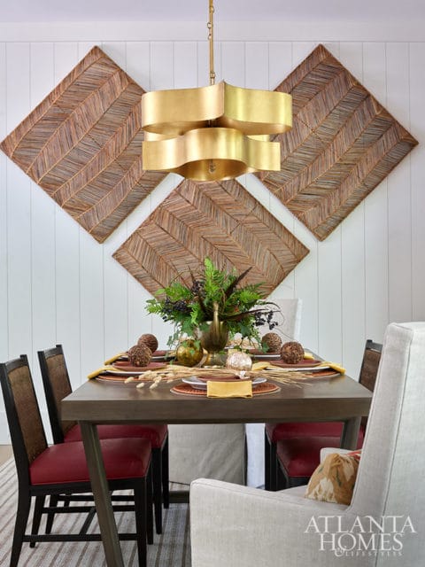 Dining room with dark wood table, red chairs, gold chandelier, and woven wall art.