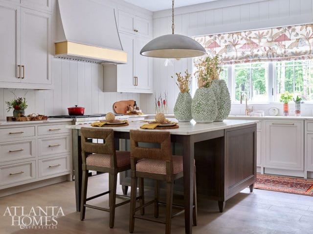 Kitchen island with two bar stools, white cabinetry, gold range hood, and patterned window