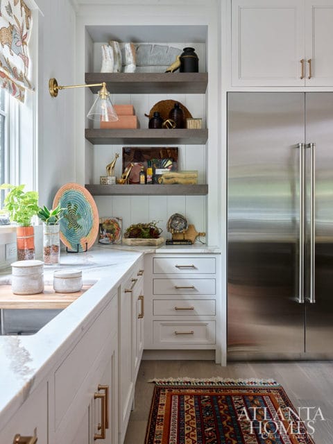 White kitchen cabinets with brass hardware, open shelves, and stainless steel refrigerator.
